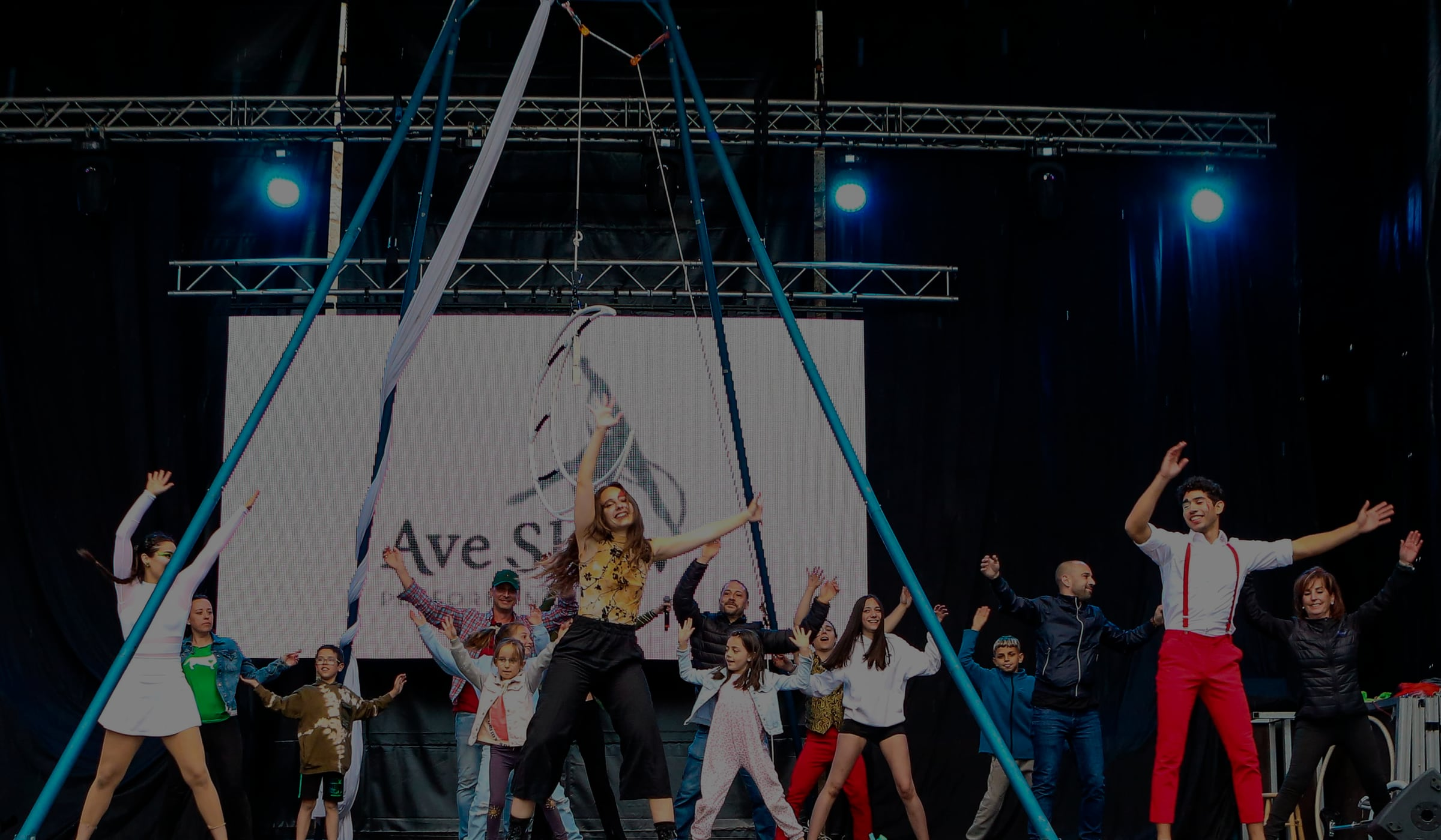 Artistas de Ave Show bailando con el público en un gran escenario con estructura de aro aéreo y telas acrobáticas